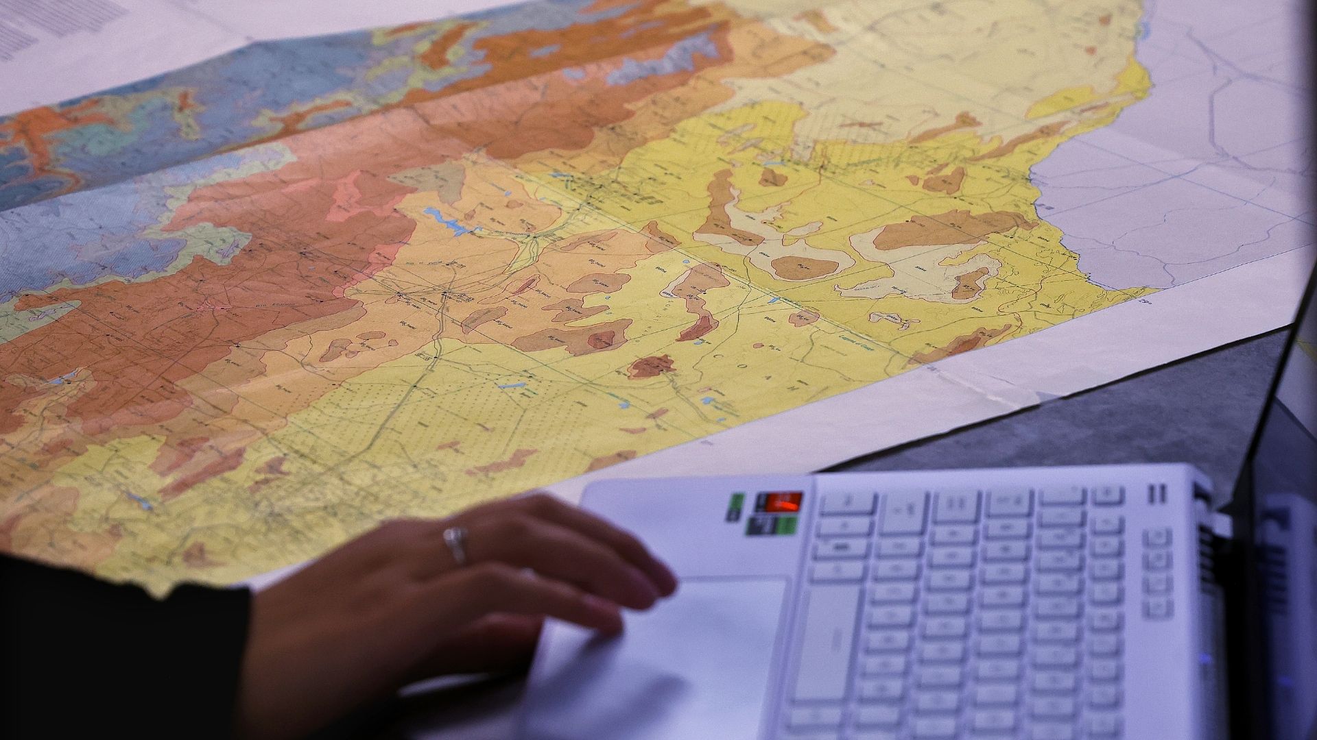 Colorful map spread out on a table, next to someone working on a computer